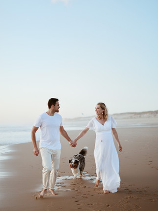 photo d'un couple qui court sur le sable avec leur chien sur la plage