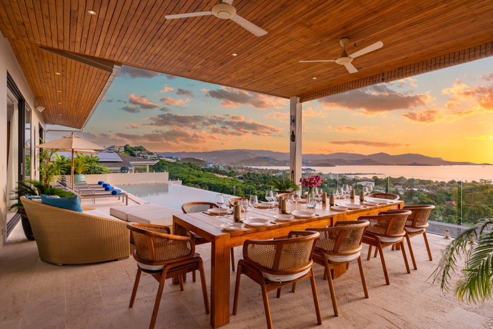 Outdoor dining table set with place settings, sunset view, and Villa Parichart.
