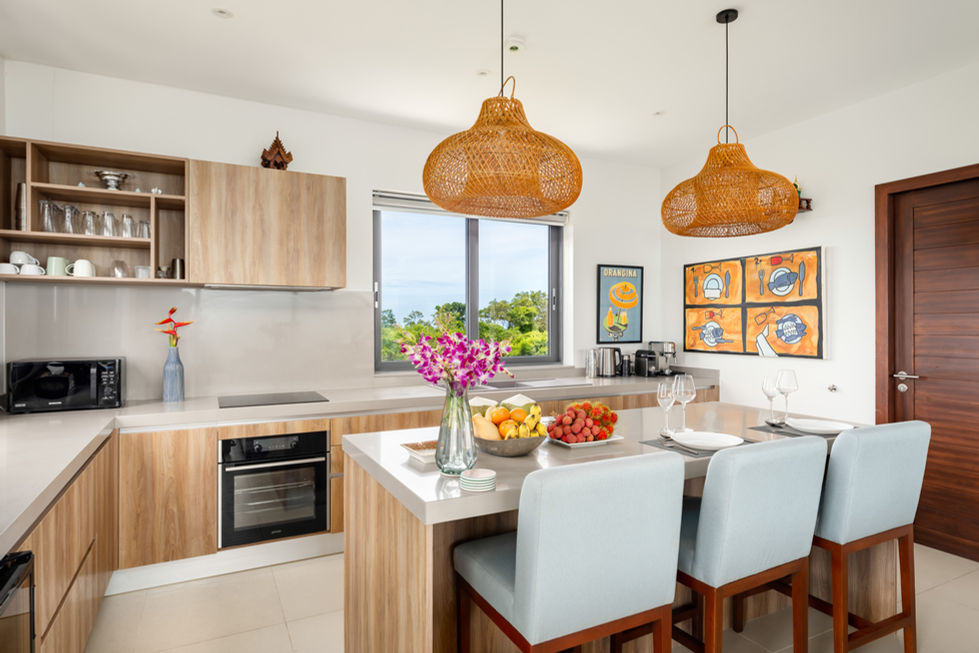 Modern kitchen with island, two chairs, pendant lights, and decorative flowers and fruits. Villa Parichart