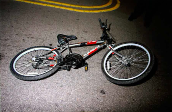 A bicycle lies on its side on a dimly lit road with yellow painted lines. The image conveys a sense of neglect or abandonment.