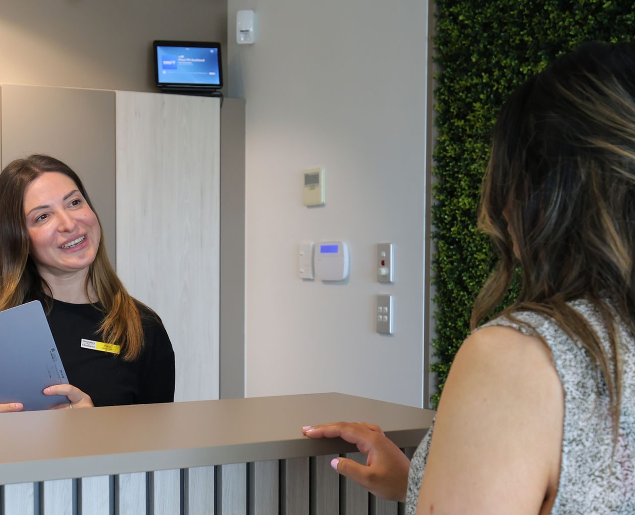 Female receptionist speaking to a female patient at the reception desk.