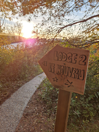 Panneau en bois « LODGE 2 DE HUVREU » sur un sentier ensoleillé, Cocoon Wood.