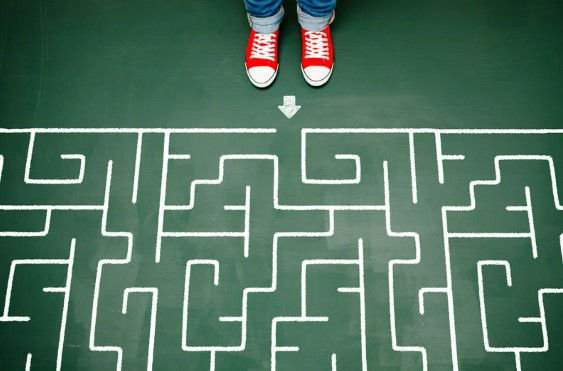 Frau mit roten Turnschuhen steht vor einem Labyrinth.
