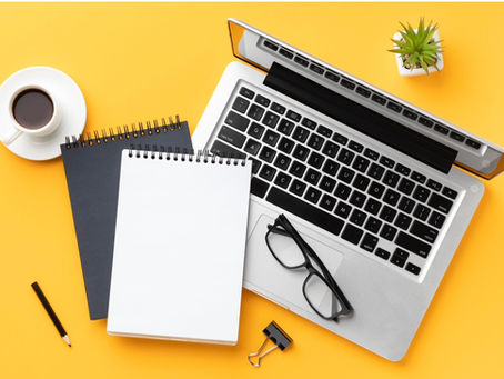 An open laptop with a cup of coffe, two notepads, a pencil, and a pair of eyeglasses.
