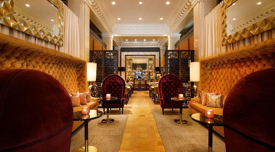 Luxurious lounge with velvet chairs, plush gold walls, and soft lighting. Candles on tables create a warm, inviting atmosphere.