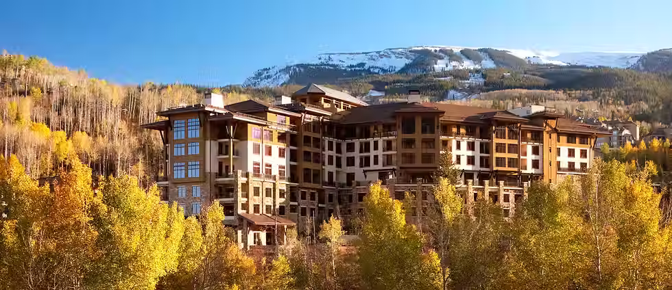 A beautiful view of The Viceroy Hotel in Snowmass, Colorado sitting a top a mountain with beautiful fall colors of orange and reds throughout all trees.