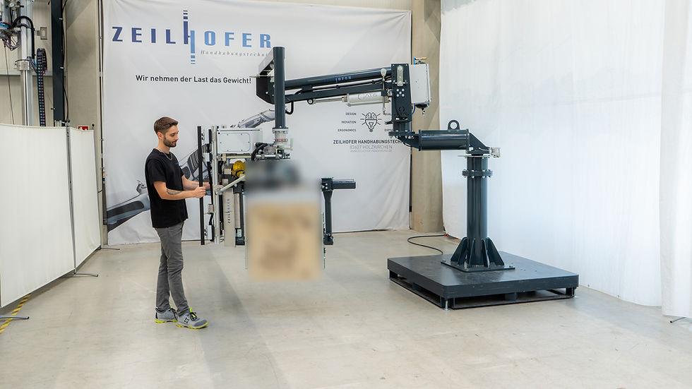 Mitarbeiter bedient einen industriellen Manipulator zum ergonomischen Handhaben und präzisen Positionieren eines schweren Sandkerns in einer Industriehalle.