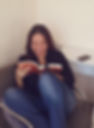 psicóloga mayara lendo um livro com sorriso, sentada em poltrona cinza, fundo branco
