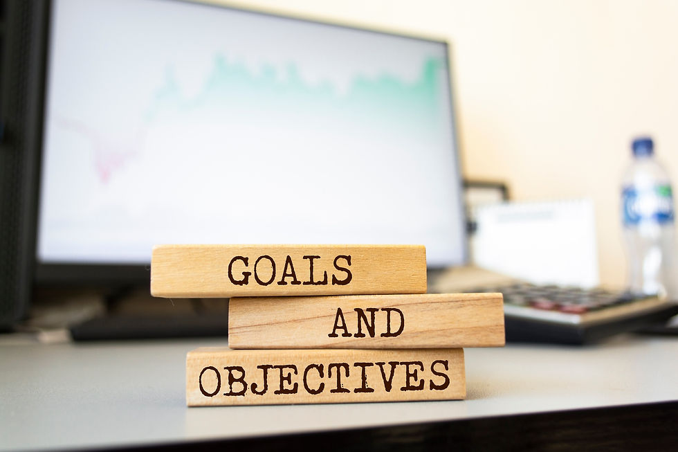 Blocks labeled "Goals and Objectives" stacked on a desk with a computer background, representing strategic planning and goal-setting in a business environment.
