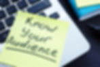 Part of a laptop keyboard with a sticky note that says "know your audience"
