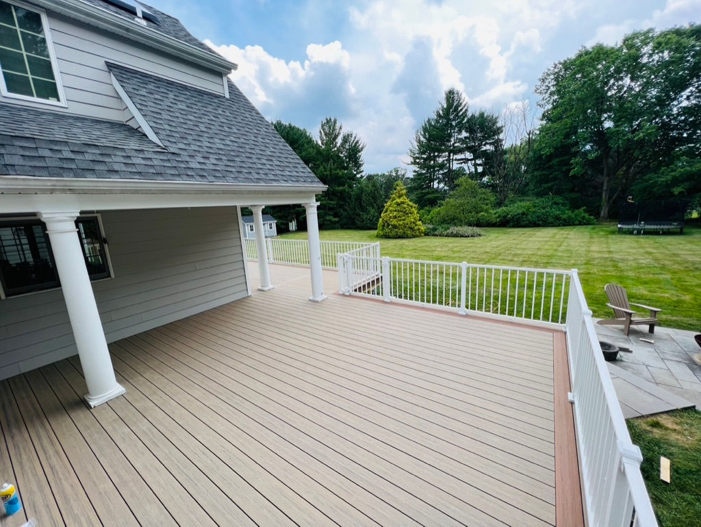 House with deck looking down to the grass in the yard with a paver patio and a trampoline in the far background.