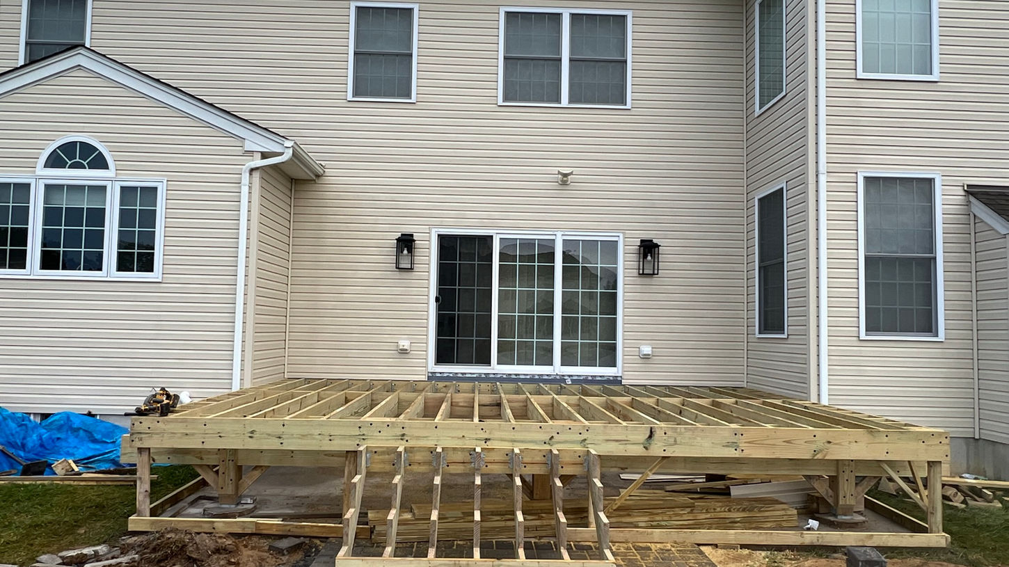 Residential deck framing and construction in progress in a New Jersey backyard, showcasing the skeleton of a new wooden deck structure with a home in the background.