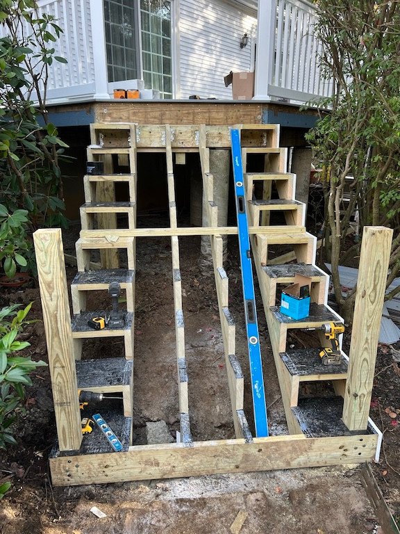 In-progress construction of wooden deck stairs surrounded by greenery.