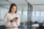 Businesswoman using Peddyl CRM on her mobile phone in a modern office setting to manage sales and customer relationships efficiently.