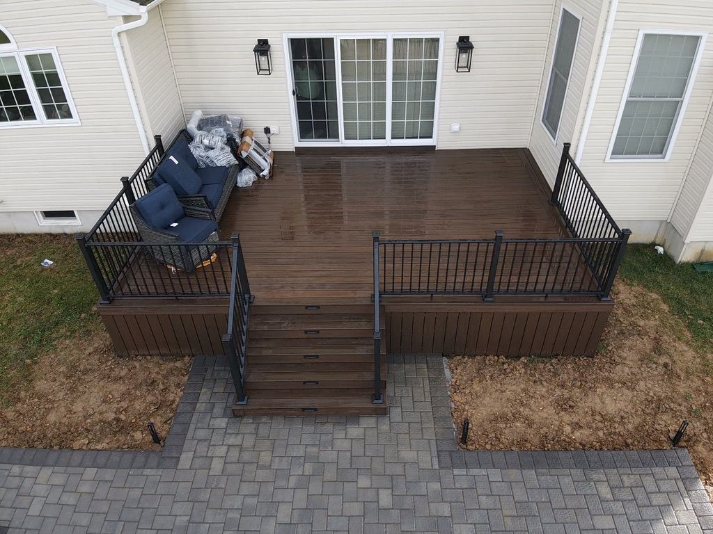 Elevated brown composite deck with black railings in a backyard, featuring outdoor furniture and paver stones.