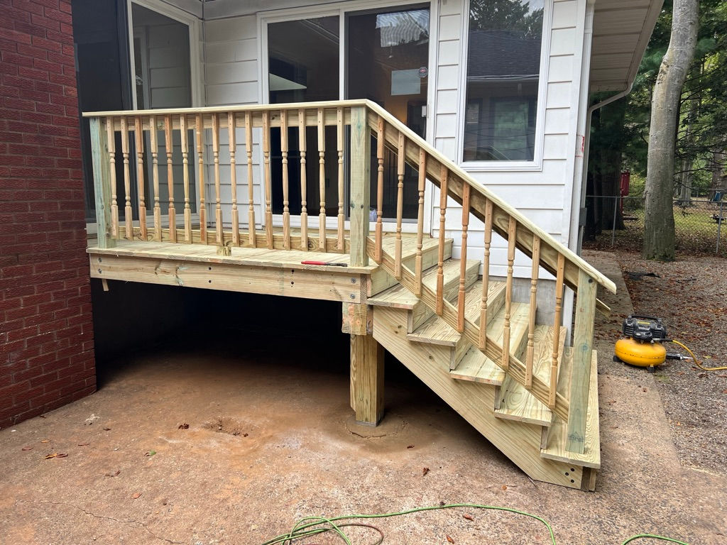 Side view of wooden deck stairs up to half sided and half brick house.