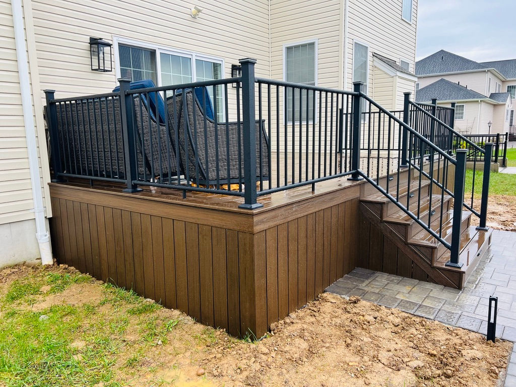 Newly installed modern composite deck with black railings and stairs at a suburban New Jersey home, showcasing a durable and stylish outdoor living space.