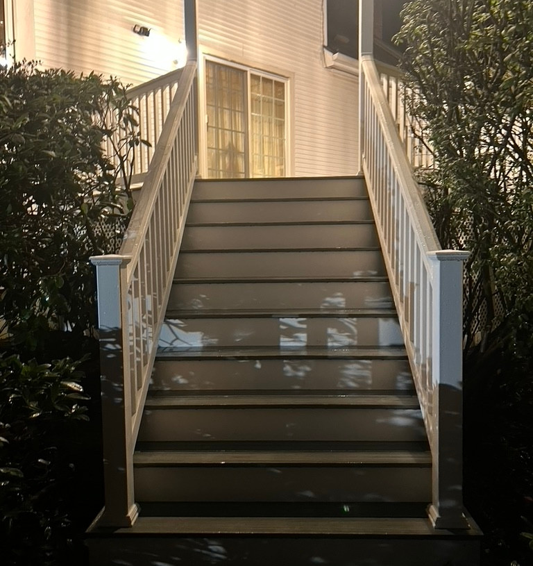 Close-up of composite decking stairs installation with railing at night time.