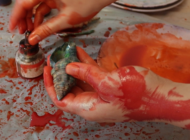 hand of an artist colored painted wth red and fluid colours and ink with seashells in a living room interior