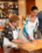 Pasta class on a floured wooden table, with dough, flour, rolling pins, and kitchen tools. A lemon and water glass are nearby.