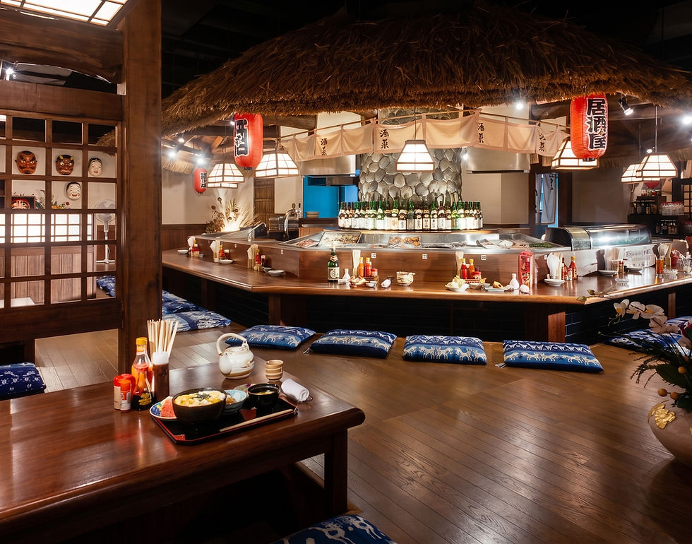 Japanese restaurant interior featuring a long sushi counter with wooden chairs, stone flooring, and an indoor tree.