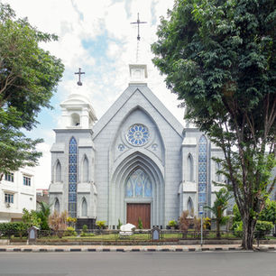 Street-level view of a grey Neo-Gothic church with pointed archways, stained-glass windows, and crosses on its bell towers.
