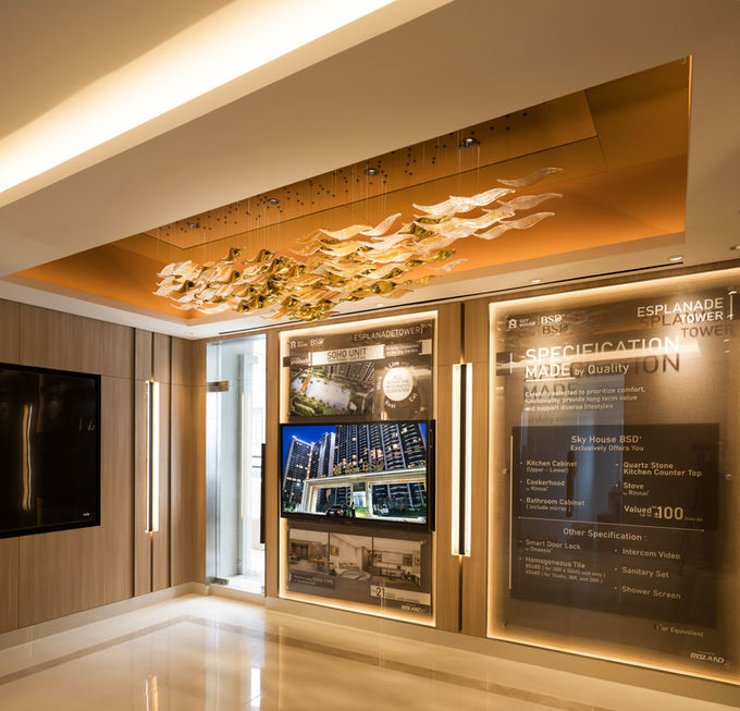 Marketing gallery featuring a large amber glass chandelier, wood-paneled walls, a TV monitor, and illuminated property specification boards.