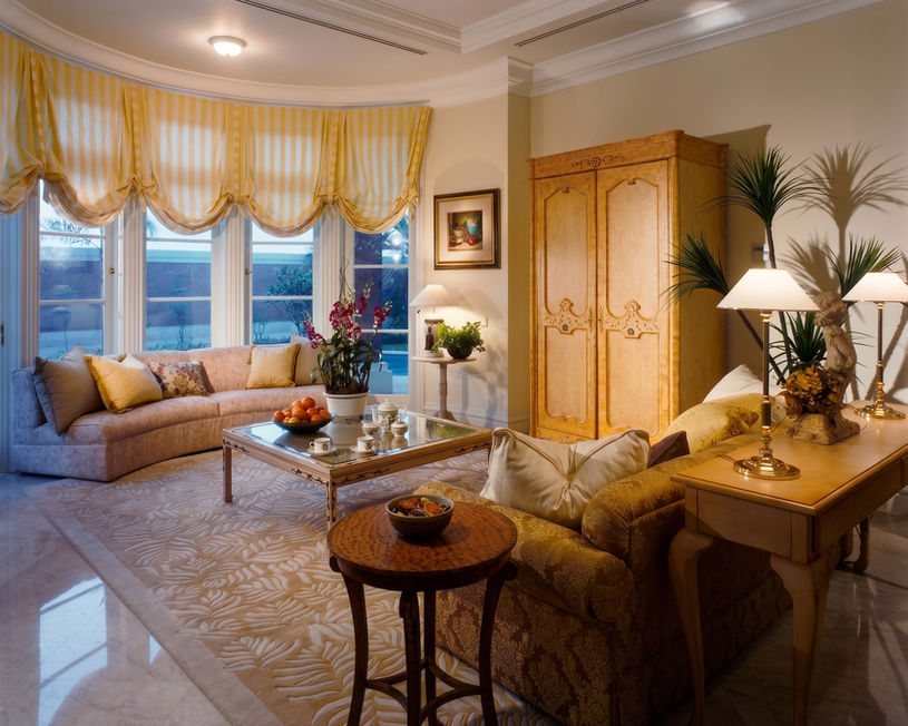 Luxurious living room interior with a large tufted sofa, classic wooden side tables, elegant lamps, and window valances.