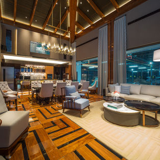 Luxurious open-plan living and dining room featuring vaulted wooden ceilings, polished patterned wood floors, a large grey sofa, and a formal dining table.