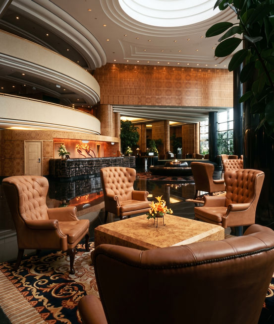 Elegant hotel lounge room featuring curved wooden walls, plush armchairs arranged around coffee tables, a patterned rug, and a grand piano in the background.