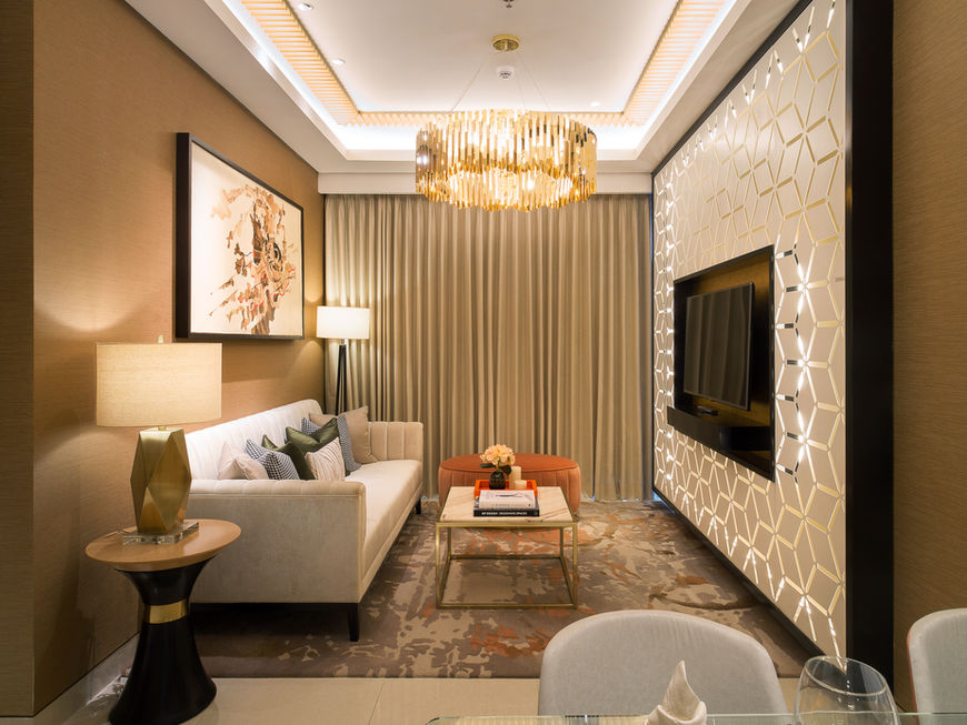 Spacious luxury living room with a large sofa, a modern chandelier, a marble TV wall, and warm lighting.