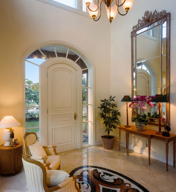 Elegant entrance foyer with high ceilings, a white arched front door, decorative marble flooring, and a classic wooden console table.