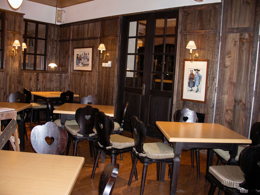 Small, dimly lit dining setup in a corner featuring striped armchairs, a wooden square table, and dark walls adorned with framed art.