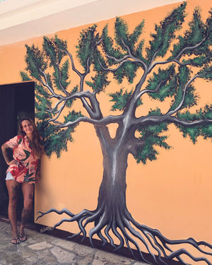 Mural of a tree on orange wall with the artist L'uba.