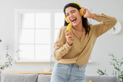 Young woman in headphones with banana singing at home