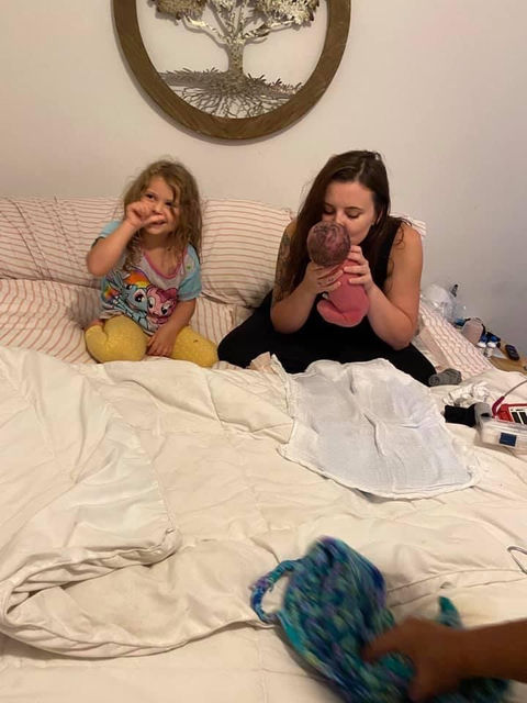 Mother and daughter with newborn while mother kisses newborn.