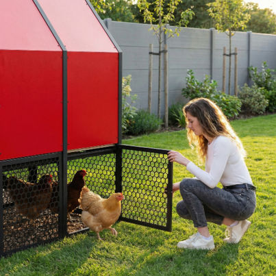 Woman opening the perforated aluminum mesh run door of the red RUN-CHICKEN Coop 2.0 as chickens step out onto grass in a modern backyard setting.