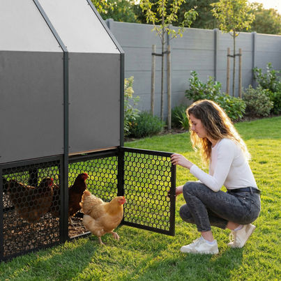 Woman opening the perforated aluminum mesh run door of the gray RUN-CHICKEN Coop 2.0 as chickens step out onto grass in a modern backyard setting.