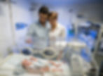 Parents stand closely together, gazing at their newborn in a NICU incubator, symbolizing the complex emotions and caregiving bonds in neonatal intensive care.
