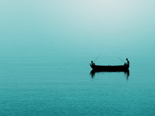 Wide image of two people fishing in a small boat on a vast, still body of teal water.
