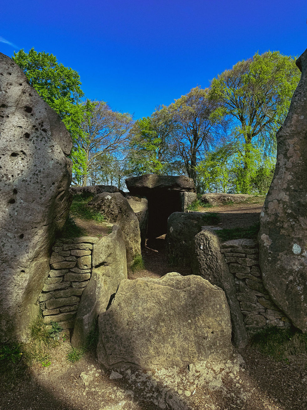 Ancient stone structure with large boulders and a path, surrounded by green trees under a clear blue sky. Peaceful and historic setting.