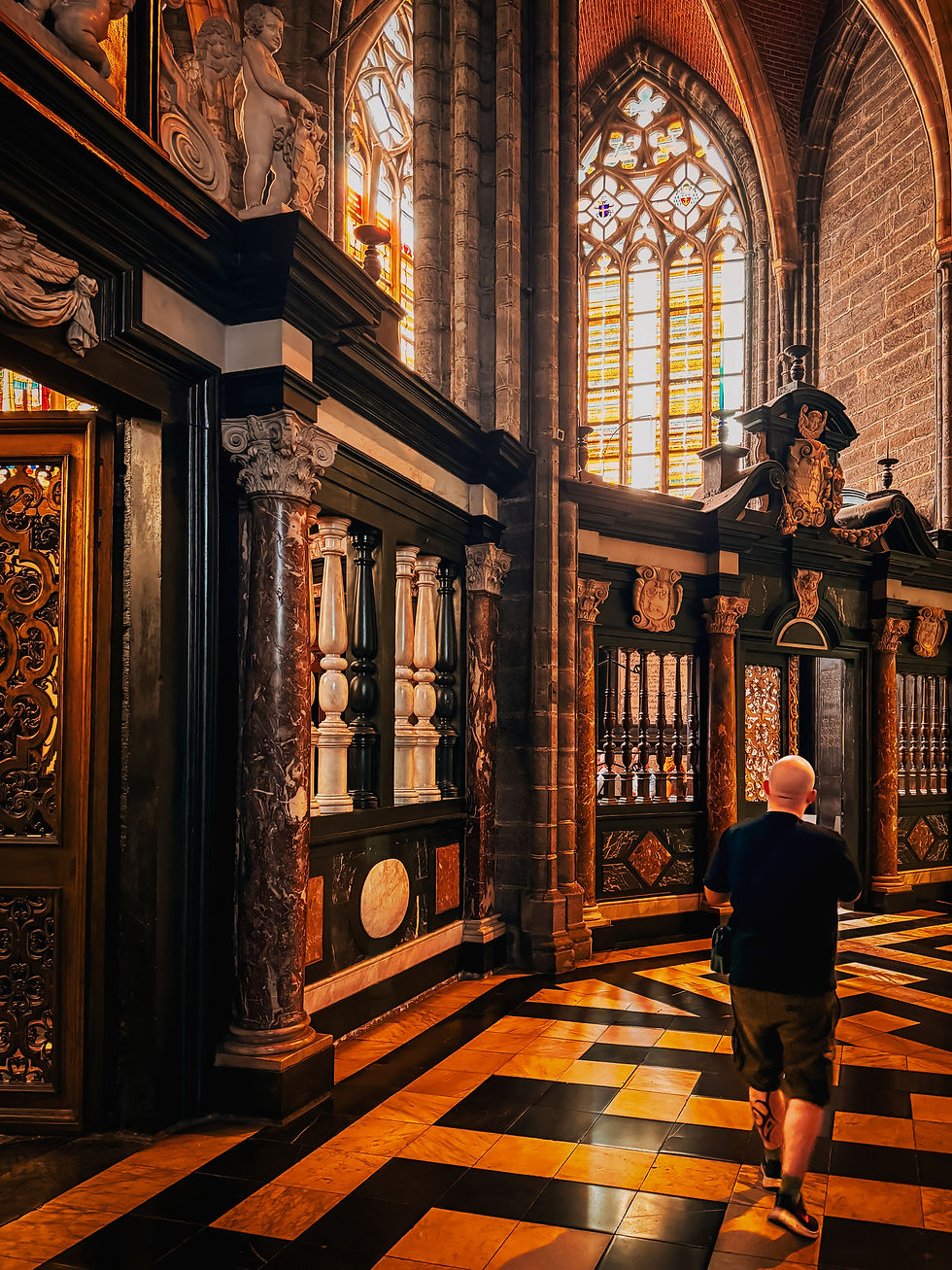 A person walks inside a cathedral with ornate columns, patterned marble floors, and colorful stained glass windows, creating a serene ambiance.