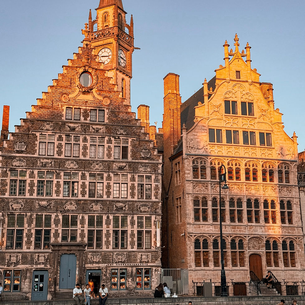 Ornate historic buildings with triangular roofs in warm sunlight, people sitting on steps, and a clock tower in the background.