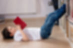 A young boy lays on his back reading a red book.