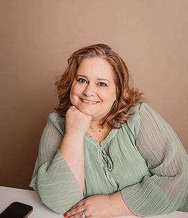 Cheree smiling in green blouse, head resting on hand at desk