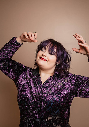 Happy smiling stylist wearing purple with her hands in the air dancing