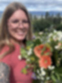 Floral Designer wearing a peach shirt, showing off her colourful bouquet with peach, white and purple flowers.