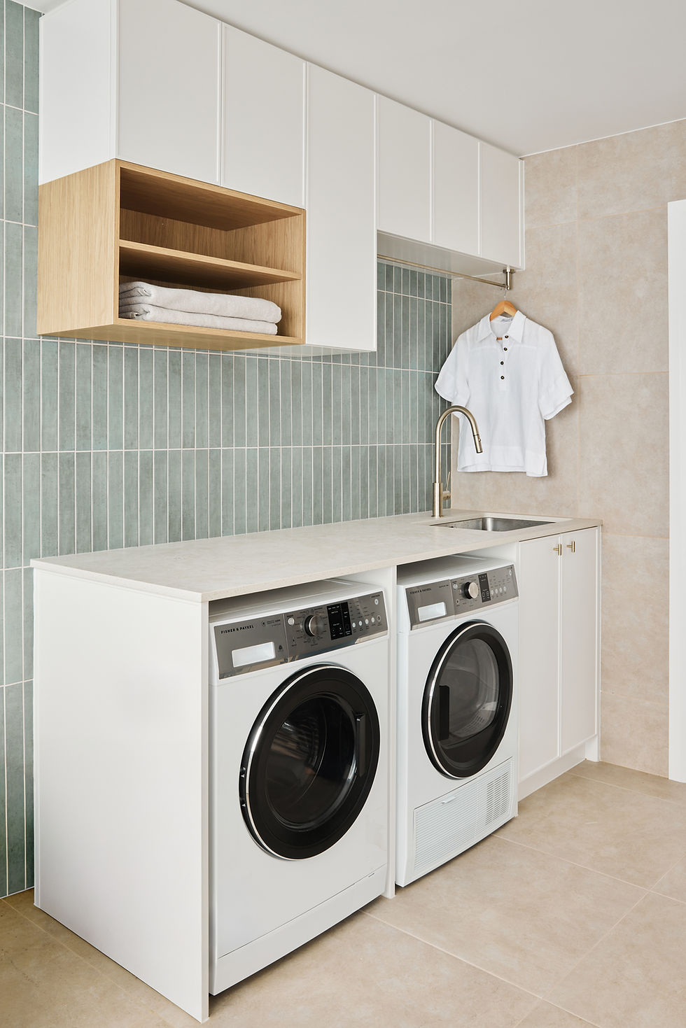 a laundry room with a washing machine and dryer, with a white shirt on a hanging rail above the sink