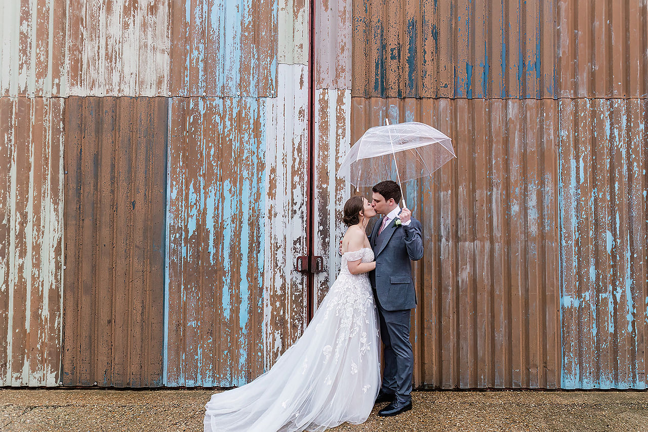 Bride and groom kissing under an umbrella at The Barns at Lodge Farm