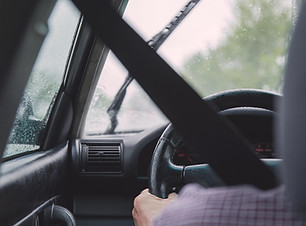 Person fährt Auto bei Regen mit Scheibenwischern auf nassem Fenster.